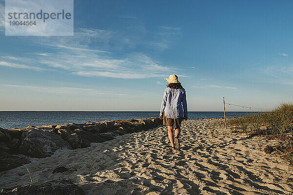 Reife Frau mit Hut spaziert im Sommer friedlich am Strand von Cape Cod