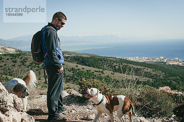 Mann lächelt Hund in den Bergen von Malaga vor blauem Himmel und Meer an