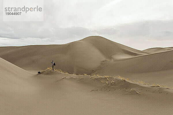 Ein männlicher Wanderer geht an einem bewölkten Tag in Colorado durch Sanddünen und Gräser