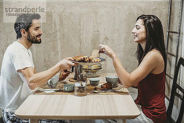 Junges glückliches verliebtes Paar beim Frühstück am Küchentisch