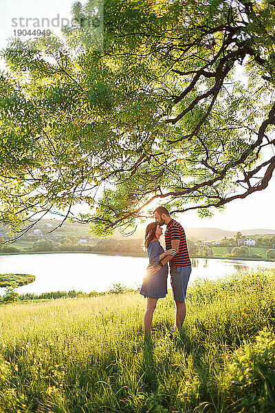 Mann und Frau stehen umarmend in einem Blumenfeld in den Strahlen der Sonne