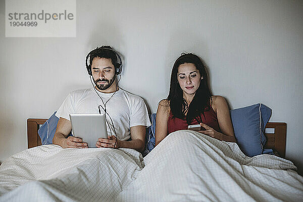 Junges Paar im Bett mit Smartphone und Tablet