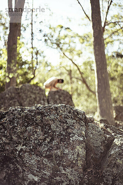Frau mit weichem Fokus kauert nackt auf einem Felsen allein in der Natur