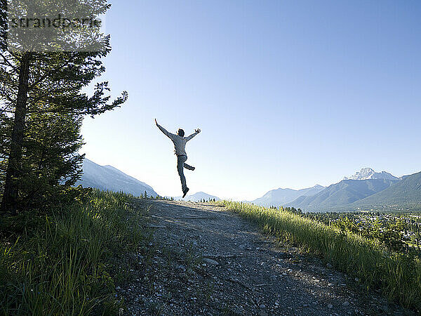 Mann springt vor Freude auf Bergpfad