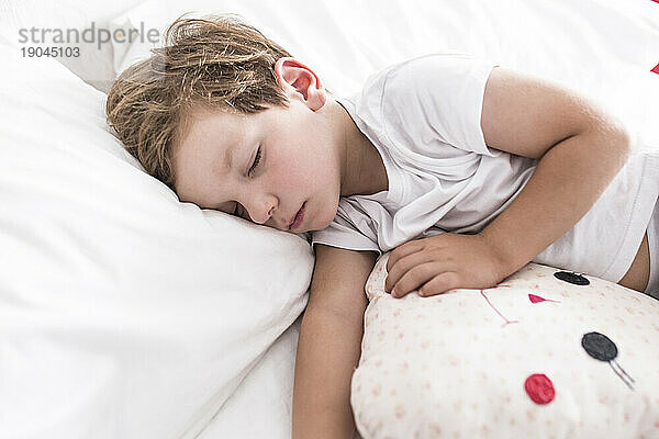 3 Jahre kleiner Junge schläft mit seinem Lieblingskissen im Bett