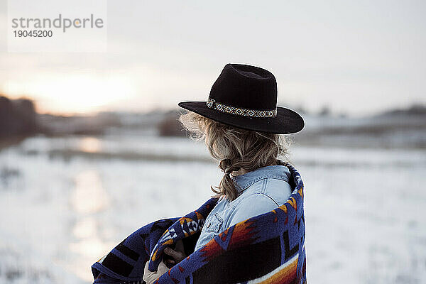Eine Frau stand mit Hut und Decke auf einem Feld und blickte in Richtung Sonnenuntergang