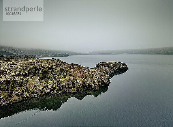 Felsen über einem ruhigen See im Nebel