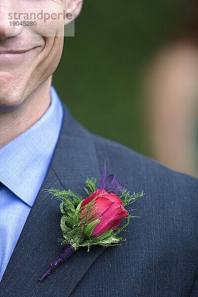 Ausgeschnittene Vorderansicht eines lächelnden jungen Mannes mit einer roten Ansteckblume am Revers.
