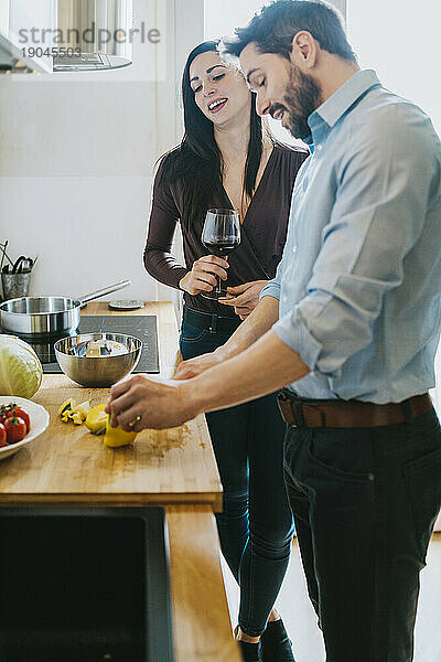 Junger Mann bereitet in der Küche das Mittagessen für seine Freundin zu  während sie ein Glas Wein trinkt