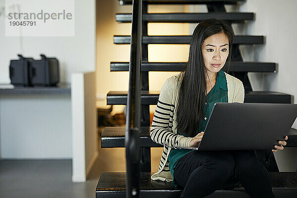 Selbstbewusste Geschäftsfrau benutzt Laptop-Computer  während sie auf Stufen im Büro sitzt