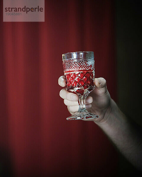 Die Hand eines Mannes hält ein Glas Rotwein vor einem roten Hintergrund.