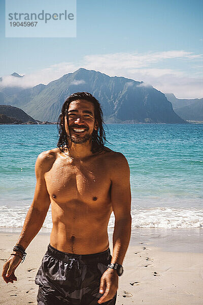 Mann mit langen Haaren lächelt nach dem Schwimmen am Strand