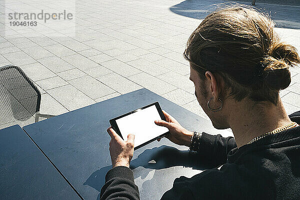 Weißer Mann mit langen Haaren mit einem Tablet-Gerät im Freien an einem sonnigen Tag