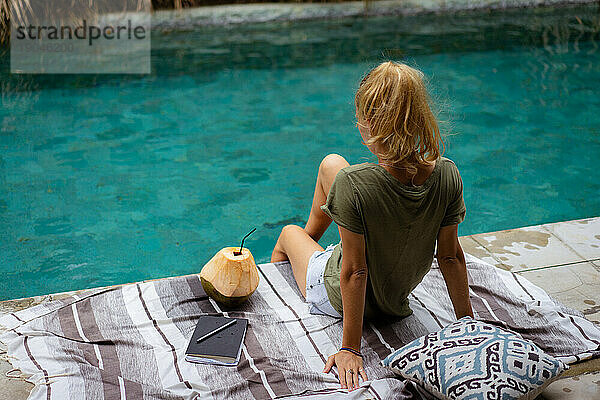 Eine junge Frau verbringt Zeit am Pool und schreibt Tagebuch.