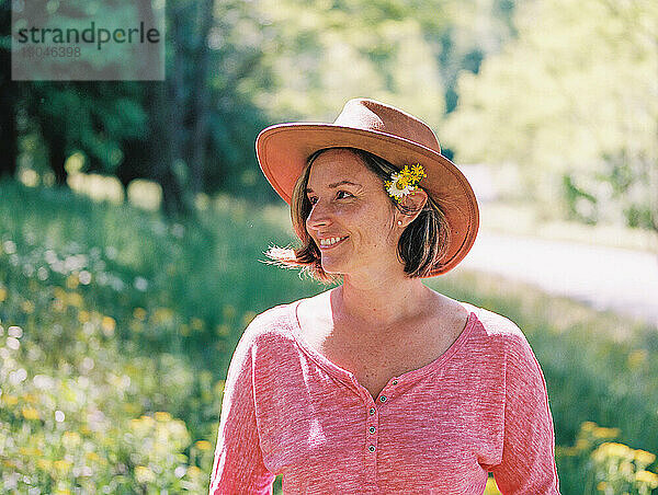 Frau mittleren Alters mit braunem Hut und Wildblumen hinter ihrem Ohr