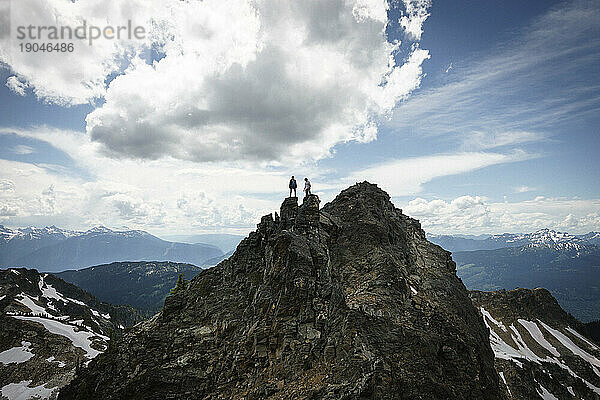 Silhouette von Mann und Frau auf dem Gipfel eines Berges mit blauem bewölktem Himmel