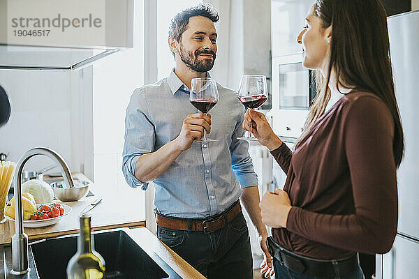 Liebespaar feiert in der Küche und stößt mit Rotwein an