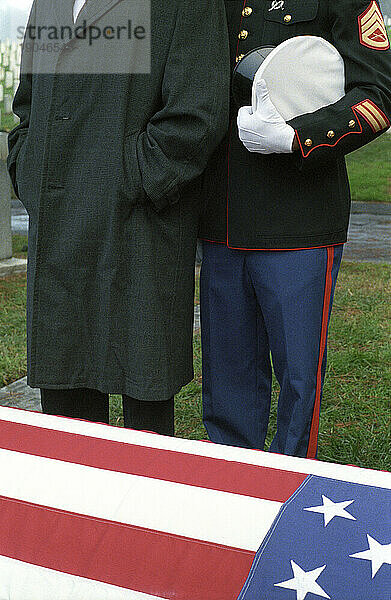 Zwei Männer erweisen an einer Grabstätte im Freien ihre letzte Ehre.