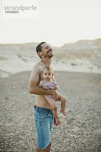 Ein Vater lacht  während er sein kleines Mädchen in der Wüste hält
