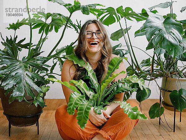 Fröhliche Millennial-Frau umarmt grüne Zimmerpflanzen