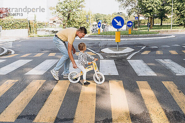 Ein Mann mit einem kleinen Mädchen überquert die Straße auf einem Laufrad