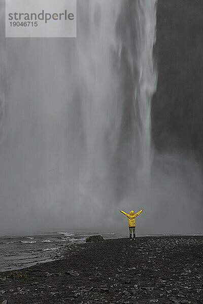 Person mit erhobenen Armen vor dem Wasserfall Skogafoss
