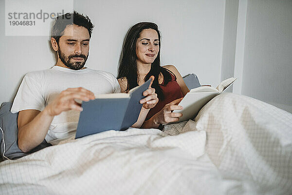 Liebespaar liest zu Hause unter der Bettdecke in einem Moment der Ruhe