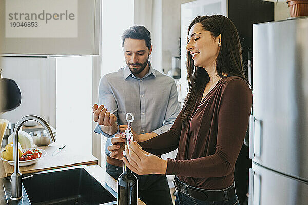 Liebespaar in der Küche. Junge Frau öffnet eine Flasche Wein