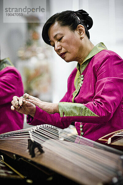 Eine Chinesin in traditioneller Kleidung spielt Gu-Zheng  ein mit den Fingern gezupftes Saiteninstrument.