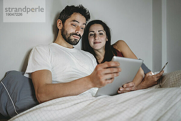 Junges Paar im Bett mit Smartphone und Tablet