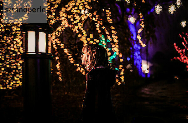 Junges Mädchen blickt nachts auf Straßenlaterne mit Weihnachtsbokeh