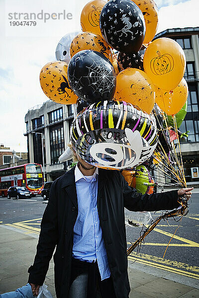 Ein Mann trägt bunte Halloween-Luftballons.