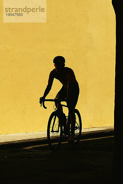 Minimalistische Silhouette eines männlichen Radfahrers vor einer schlichten gelben Wand