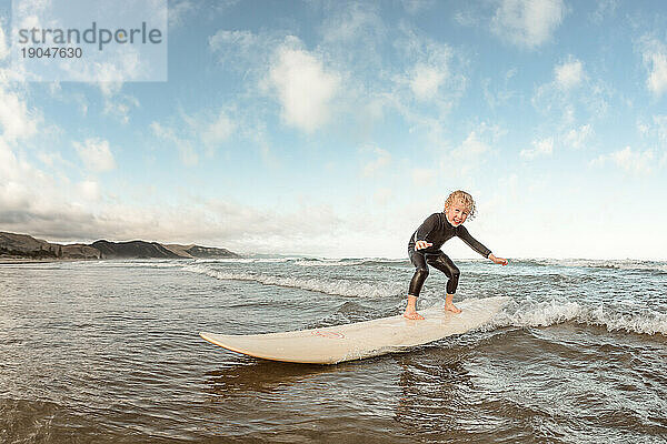 Kleines Kind surft an einem sonnigen Tag am Strand auf einem Surfbrett