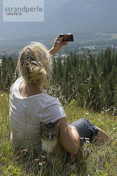 Frau macht Foto mit Katze auf Bergwiese