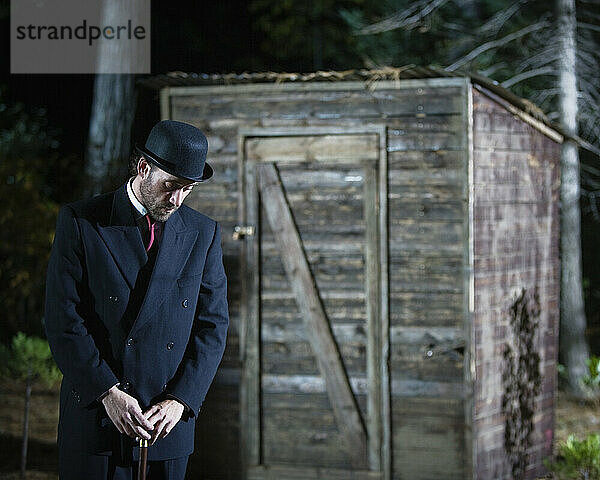 Ein Mann steht nachts vor einem Holzschuppen.