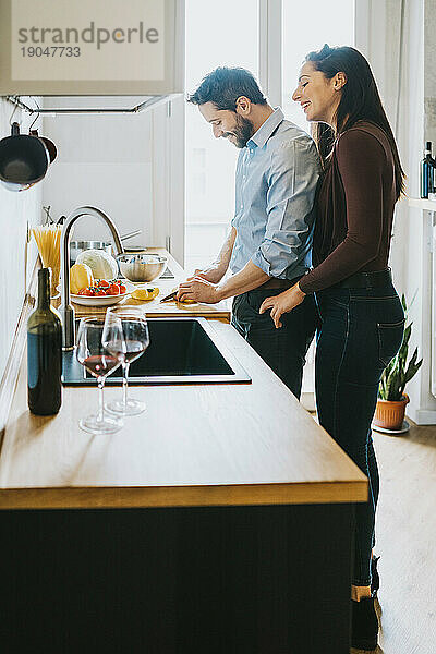 Junger Mann bereitet in der Küche das Mittagessen für seine Freundin zu  während sie ein Glas Wein trinkt