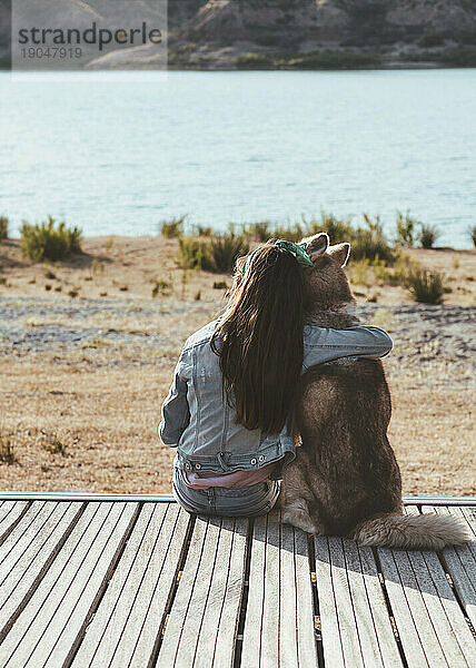 Ein Mädchen saß an einem See und umarmte ihren Husky und beobachtete den Sonnenuntergang
