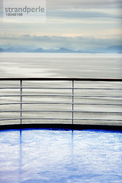 Kreuzfahrtschiffdeck und Pool mit Geländer und Meer im Hintergrund.