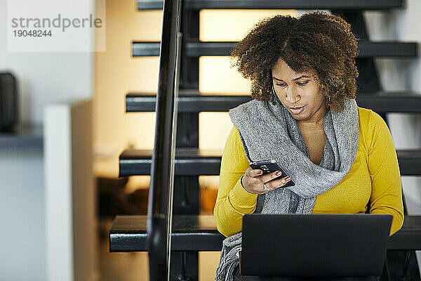 Geschäftsfrau mit Laptop-Computer und Mobiltelefon  während sie auf Stufen im Büro sitzt