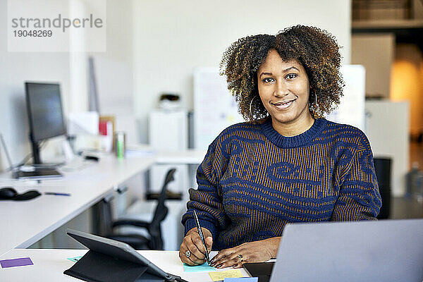 Porträt einer selbstbewussten Geschäftsfrau mit lockigem Haar  die im Büro auf Klebezettel schreibt