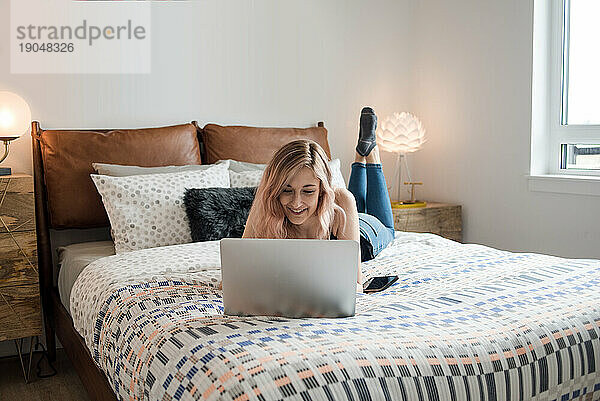 Junge Frau liegt mit Laptop im Bett