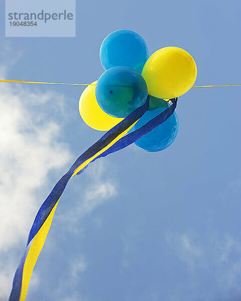 Blaue und gelbe Luftballons vor einem bewölkten blauen Himmel.