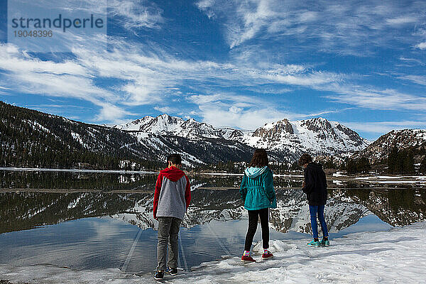 Der Rücken von drei Kindern an einem zugefrorenen See mit schneebedeckten Bergen