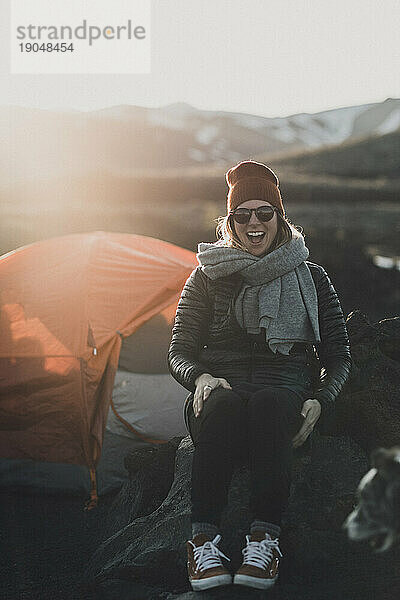 Eine Camperin lacht laut auf einem Campingplatz bei kaltem Sonnenuntergang