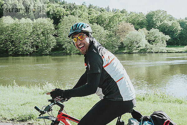 Lächelnder Radfahrer  der mit seinem Fahrrad in der Nähe des Flusses fährt