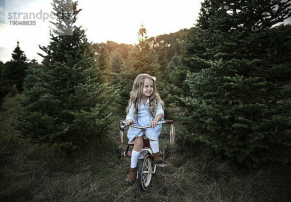 Kleines Mädchen lächelt auf dem Fahrrad mit Weihnachtsbäumen