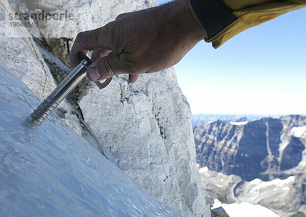 POV der Hände eines Bergsteigers  der eine Eisschraube über den Bergen setzt