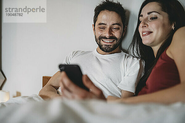 Junges Paar im Bett und schaut auf das Smartphone