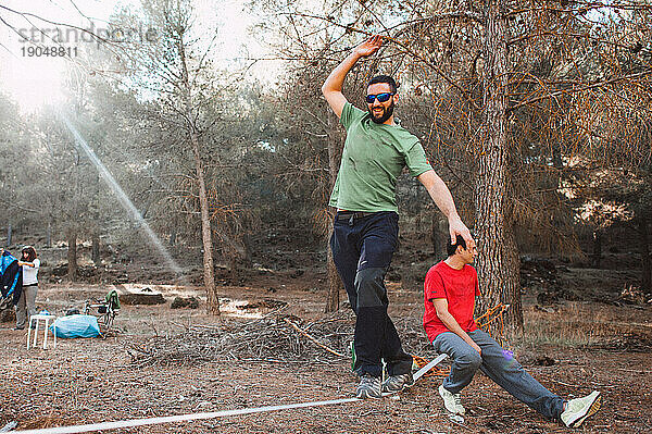 Mann beim Slacklinen mit Freunden im Wald an einem sonnigen Tag in Spanien